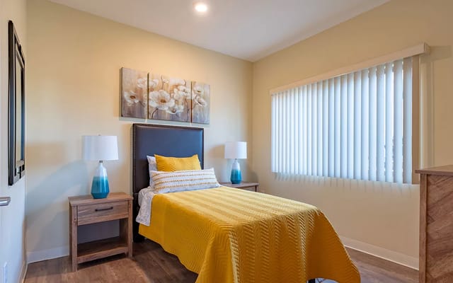 Bedroom with a yellow quilt, lamps, and decorative wall art