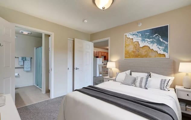 A well-decorated bedroom with a bed, bedside tables, and a bathroom entry
