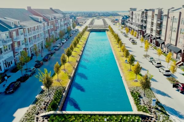 Aerial view of a landscaped waterway flanked by trees and residential buildings.