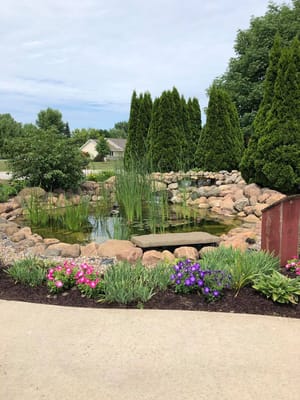 A serene garden pond surrounded by lush greenery and colorful flowers.