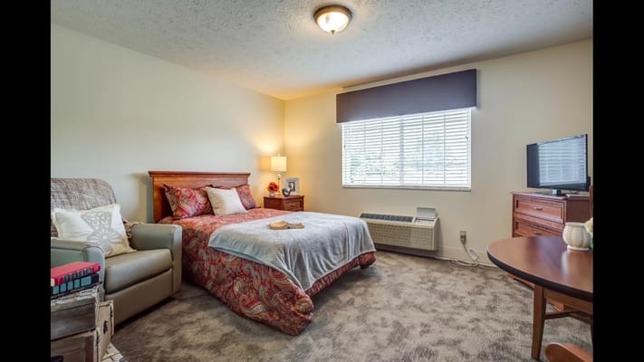 A cozy bedroom featuring a bed, armchair, and TV.