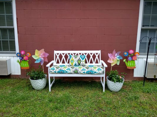 A white bench with colorful pillows and decorative planters against a brown wall.