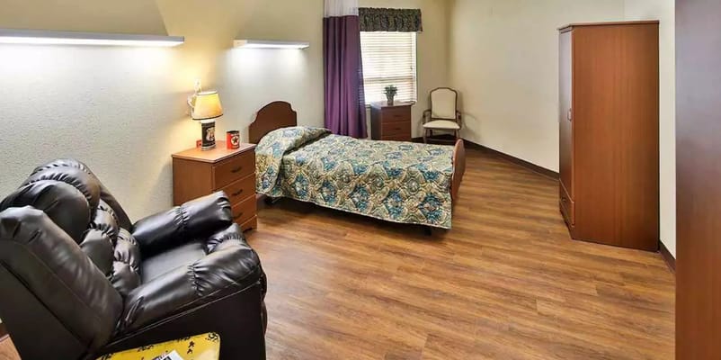 A cozy bedroom featuring a bed, recliner, and wooden furniture.