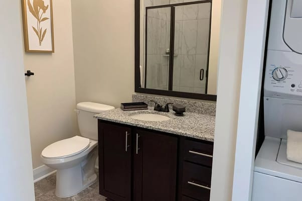 Modern bathroom featuring a shower, toilet, and sink with granite countertop.