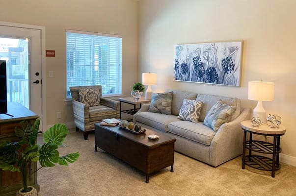 Living room with a couch, armchair, and decorative table in a senior living facility.