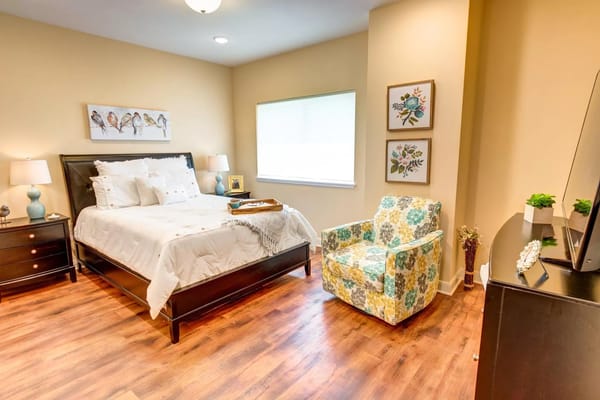 A well-decorated bedroom with a bed, patterned chair, and window.