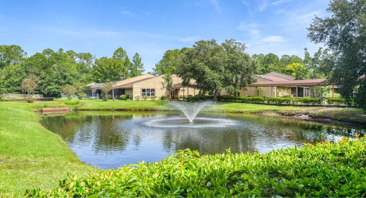 Pond with fountain surrounded by greenery and building