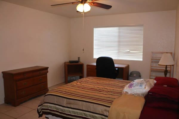 A cozy bedroom with a striped bedspread, desk, and dresser.