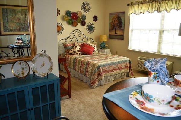A cozy bedroom featuring a colorful quilt, decorative wall art, and a reflection in a mirror.