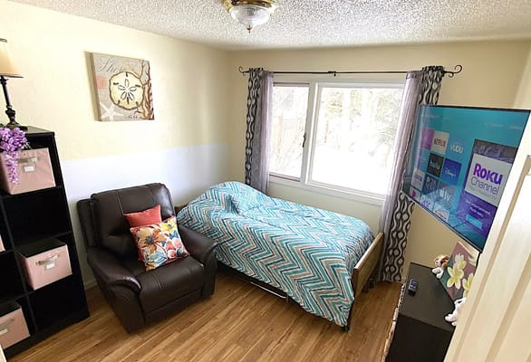 Comfortable bedroom featuring a bed, chair, and TV in Family Care Assisted Living facility.