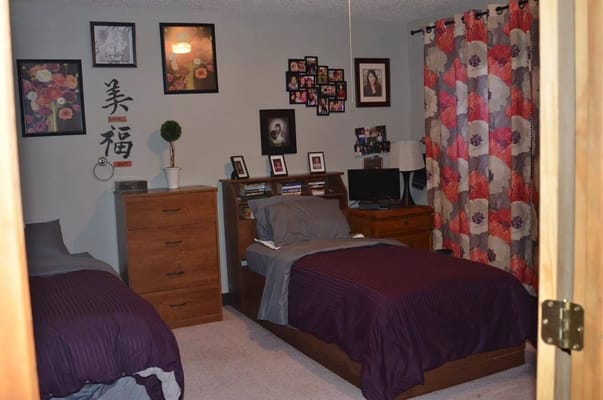 A bedroom with two beds, floral curtains, and personal decor
