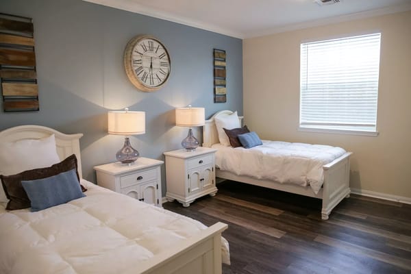 A cozy bedroom with two beds, lamps, and decorative clock on the wall.