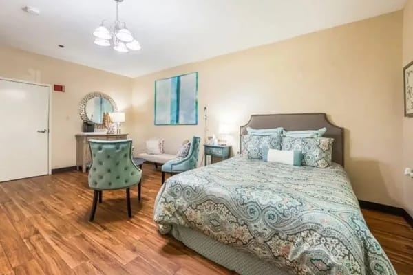 A well-decorated bedroom with a queen-sized bed, chair, and dressing table.