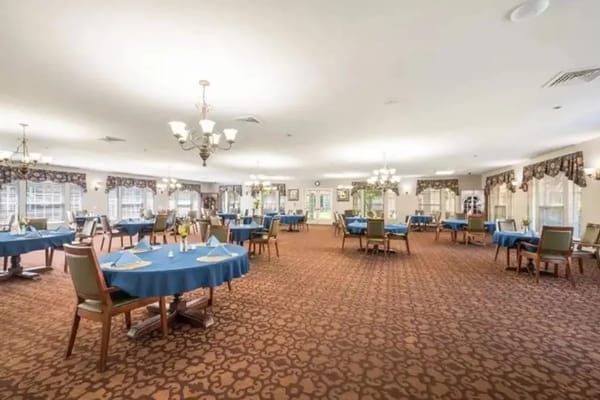 A spacious dining room with round tables and blue tablecloths.