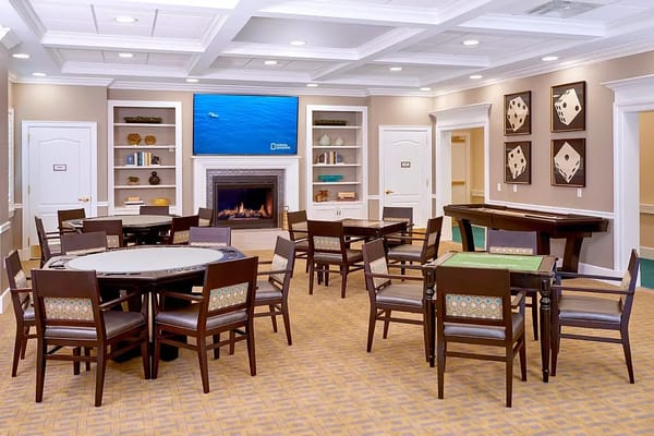 A spacious common area featuring tables and chairs, a fireplace, and a television.