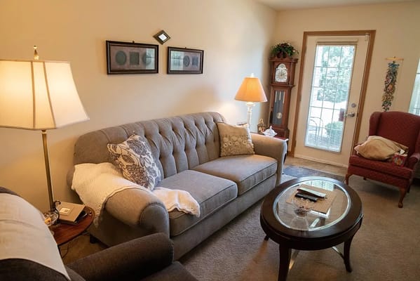A comfortable living room with a gray couch, lamp, and glass-topped coffee table.