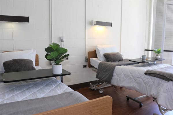 Two hospital beds with side tables in a patient room