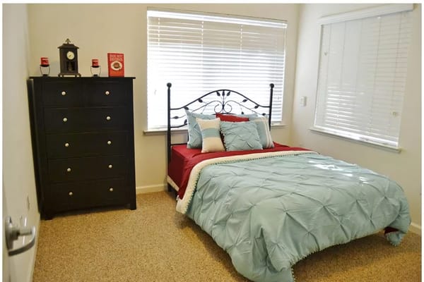 A neatly arranged private resident bedroom with a bed and dresser