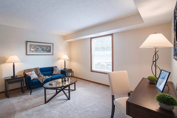 A comfortable living room with a blue couch, coffee table, and a workspace.
