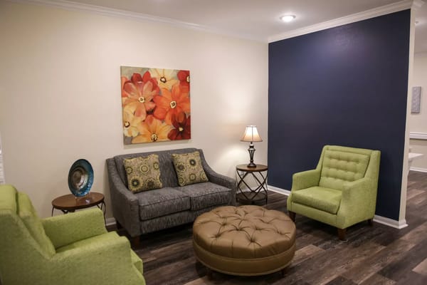 Cozy living room with green armchairs, a gray sofa, and floral artwork.