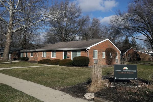 A brick building at Stafford Village surrounded by grass and trees.