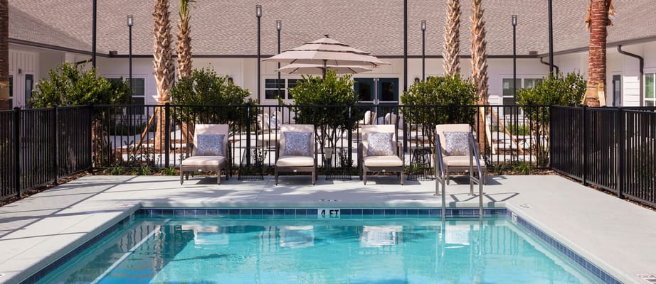 Outdoor pool area with lounge chairs and umbrellas at Senior Living at the Greens