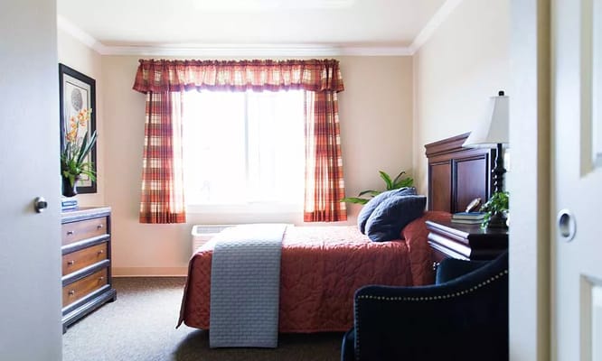 A bright private bedroom featuring a bed, dresser, and window with curtains.