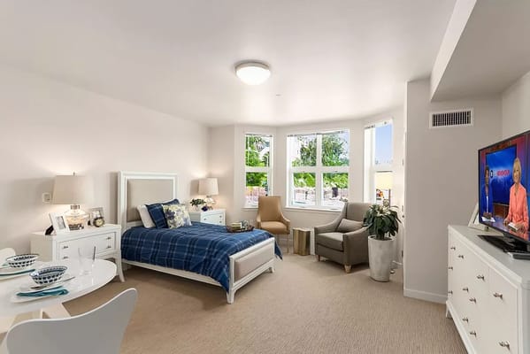 Brightly lit bedroom with a bed, armchair, and TV
