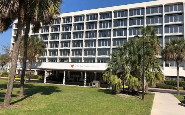 Front view of The Rose Garden senior living facility with palm trees