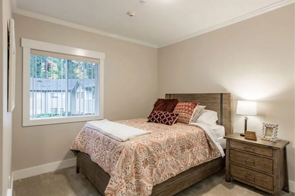 A cozy bedroom with a bed, decorative pillows, nightstand, and window.