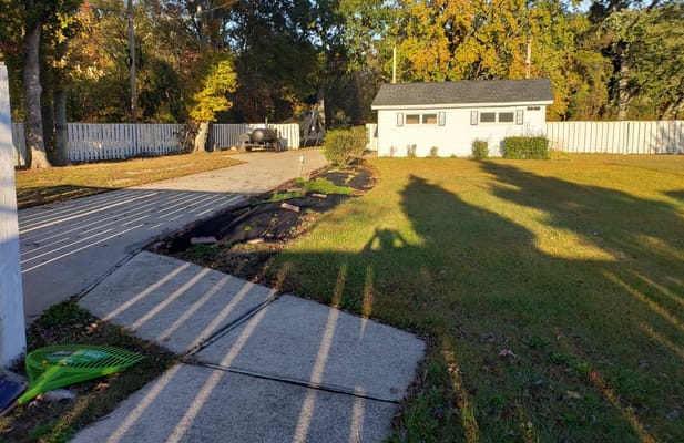 Pathway with shadows and garden beds leading to a small building.