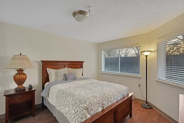 A cozy bedroom with a bed, lamp, and windows