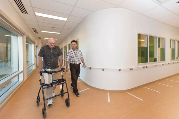 A senior resident walking with staff in a bright hallway