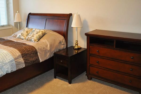 A well-furnished bedroom featuring a wooden bed, nightstand, dresser, and decorative pillows.