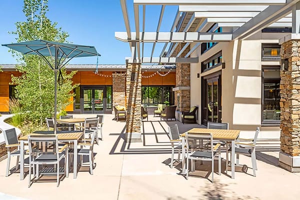 A sunny outdoor patio with tables, umbrellas, and greenery at Sagewood at Daybreak.