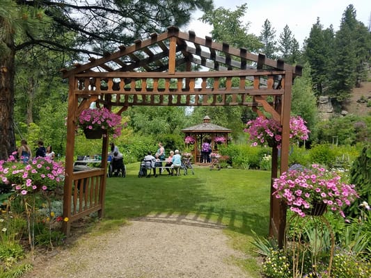A garden with a wooden arbor and vibrant flowers, featuring residents gathered around tables.