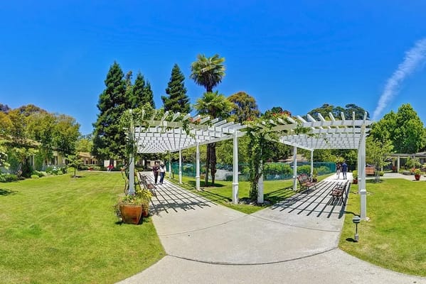 A sunny garden pathway with a pergola at Silverado Belmont Hills Memory Care Community.