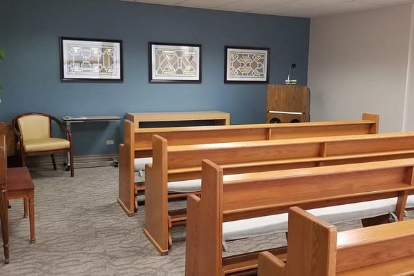 Chapel seating area with wooden benches and art on walls.