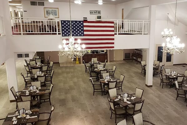 Spacious dining room with tables set for meals and a large American flag.