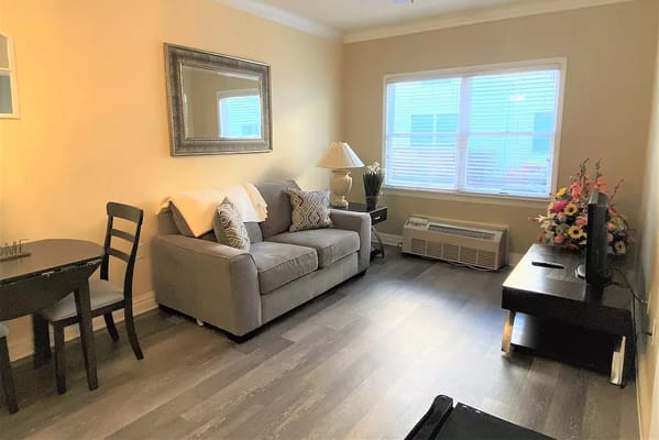 A cozy living room featuring a grey sofa, a dining table, and a window with natural light.