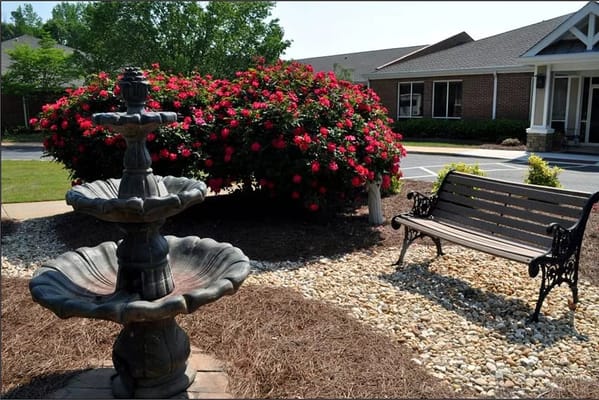 Stone fountain surrounded by flowers and a bench