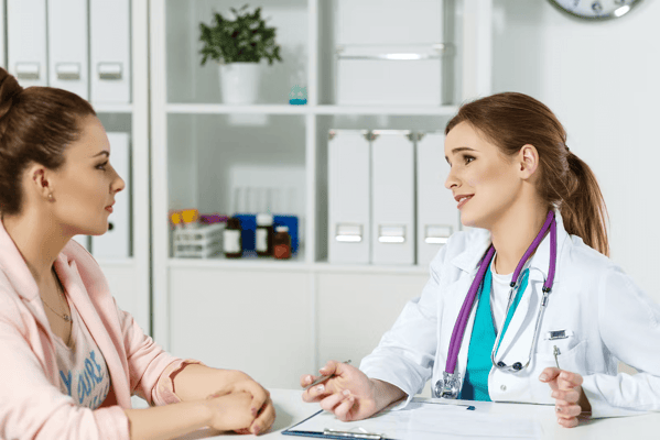 A healthcare professional in a white coat conversing with a patient at a table.