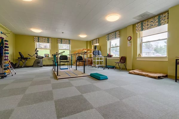 A therapy room with exercise equipment and seating at St. Vincent De Paul Nursing Home.