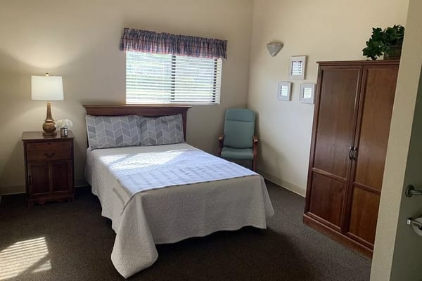 A well-lit bedroom featuring a bed, lamp, and comfortable chair.