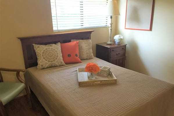 A neatly arranged bedroom with a bed, decorative pillows, and a bedside table.