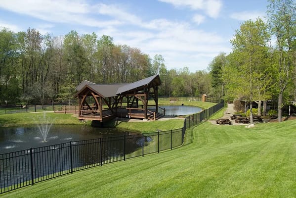 A pond with a gazebo surrounded by green grass and trees at Tanglewood Manor.
