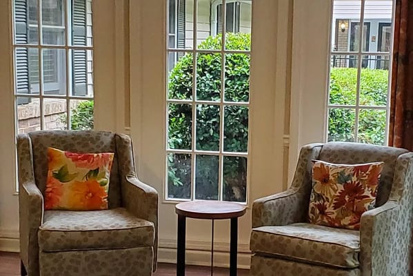 Two comfortable chairs with floral pillows beside a small table and large windows