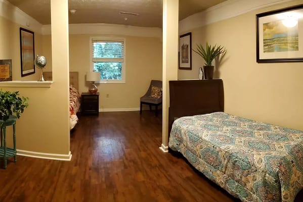Interior view of a shared room in Tapestry House Memory Care, featuring two beds and warm decor.