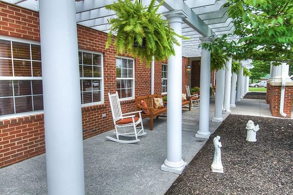 Patio area with rocking chairs and greenery at Pheasant Ridge Nursing and Rehab Center