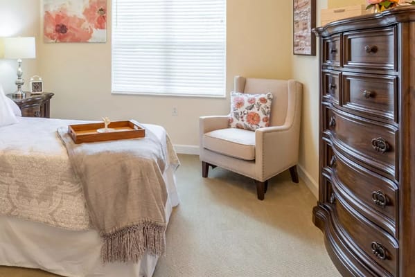 A cozy bedroom featuring a bed, wooden dresser, and comfortable armchair.